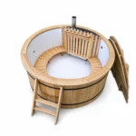 Ronde houten hottub met witte kuip, gebogen houten binnenbank, interne houtkachel achter een houten beschermrek, rechte metalen schoorsteen, houten ladder en rechtopstaande tweedelige houten afdekking op witte achtergrond.