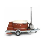 TimberIN Nordic Mobile ronde houtgestookte hottub op een eenassige aanhanger met lichte kuip, roodbruine houten bekleding, houten trap, externe roestvrijstalen kachel en schoorsteen op witte achtergrond.