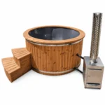 TimberIN Nordic External Comfort ronde houten hottub met donkergrijze kuip, houten opstap en externe roestvrijstalen houtkachel met hoge schoorsteen en geperforeerd hitteschild op witte achtergrond.