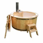 TimberIN Nordic Snorkel Compact ronde houten hottub met lichte kuip, geïntegreerde houtkachel achter een houten beschermrek, hoge schoorsteen met geperforeerd hitteschild, los geplaatste tweedelige houten afdekking en houten opstap op witte achtergrond.