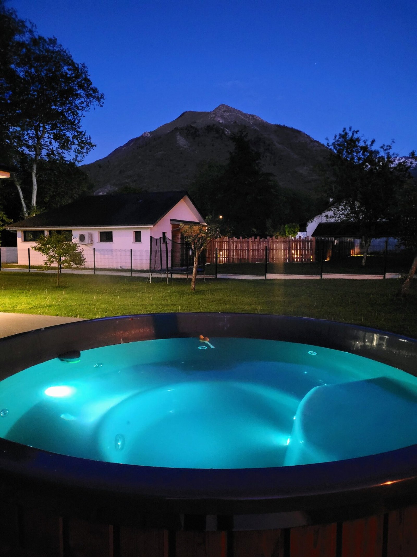 Ronde hottub met verlicht blauw water in de tuin bij schemering
