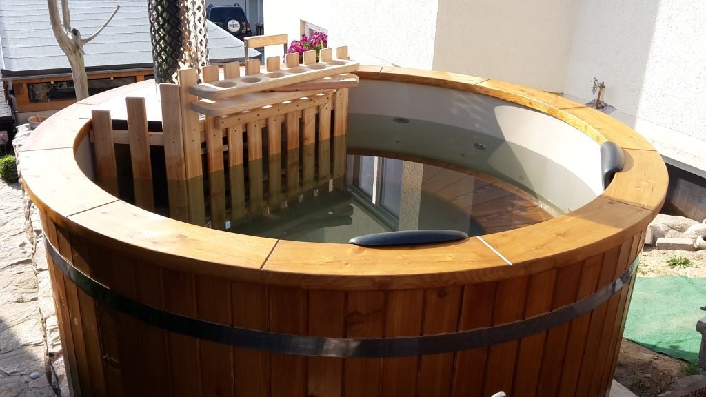 Archiefbeeld van een hottub met houten buitenrand, lichte binnenkuip en kachelafscherming