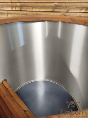 Blik in de lege rvs binnenkuip van het TimberIN Icetub-koudwaterbad, met geborstelde metalen wand, ronde bodem en kleine houten zitstap links