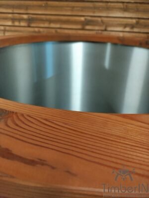 Close-up van de ronde rand van het TimberIN Icetub-koudwaterbad, met geborstelde rvs binnenkuip en brede, fijn generfde thermohouten rand