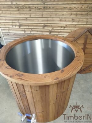 Verhoogd vooraanzicht van het open TimberIN Icetub-koudwaterbad, met rvs binnenkuip, thermohouten rand, twee aftapkranen en daarachter een leunende houten afdekking