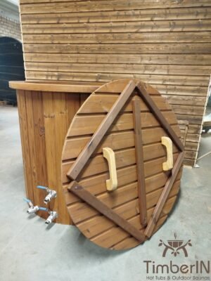Vooraanzicht van het TimberIN Icetub-koudwaterbad met thermohouten bekleding, twee aftapkranen en een ronde houten afdekking met handgrepen tegen het bad