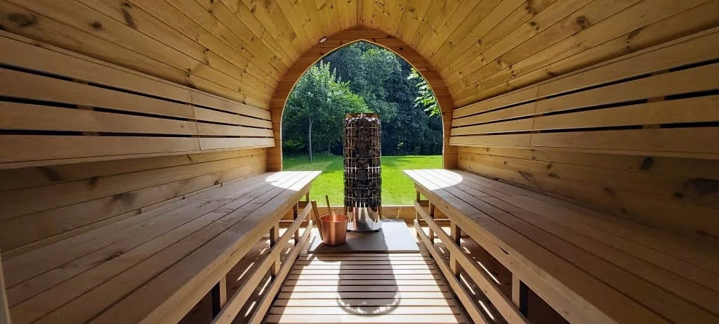Houten sauna-interieur met banken, kachel en uitzicht op de tuin