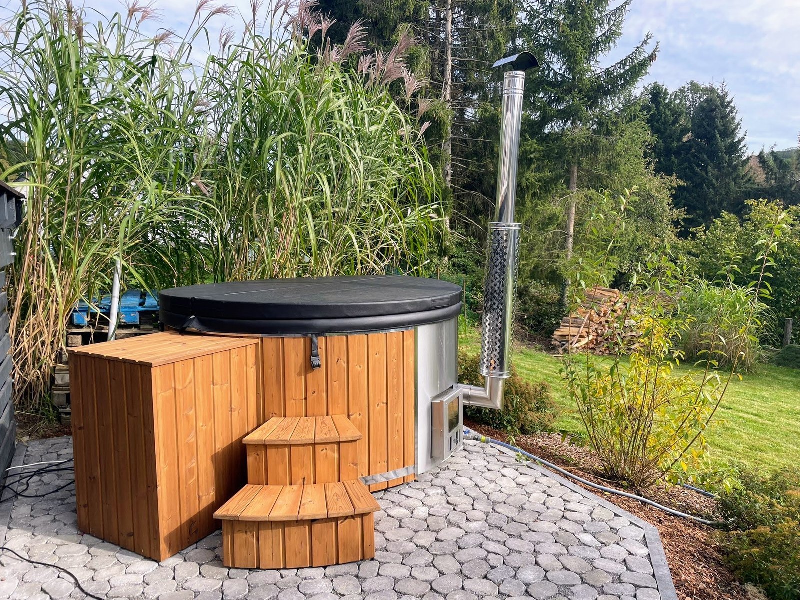Houtgestookte hottub met houten bekleding, deksel en trap in een tuin