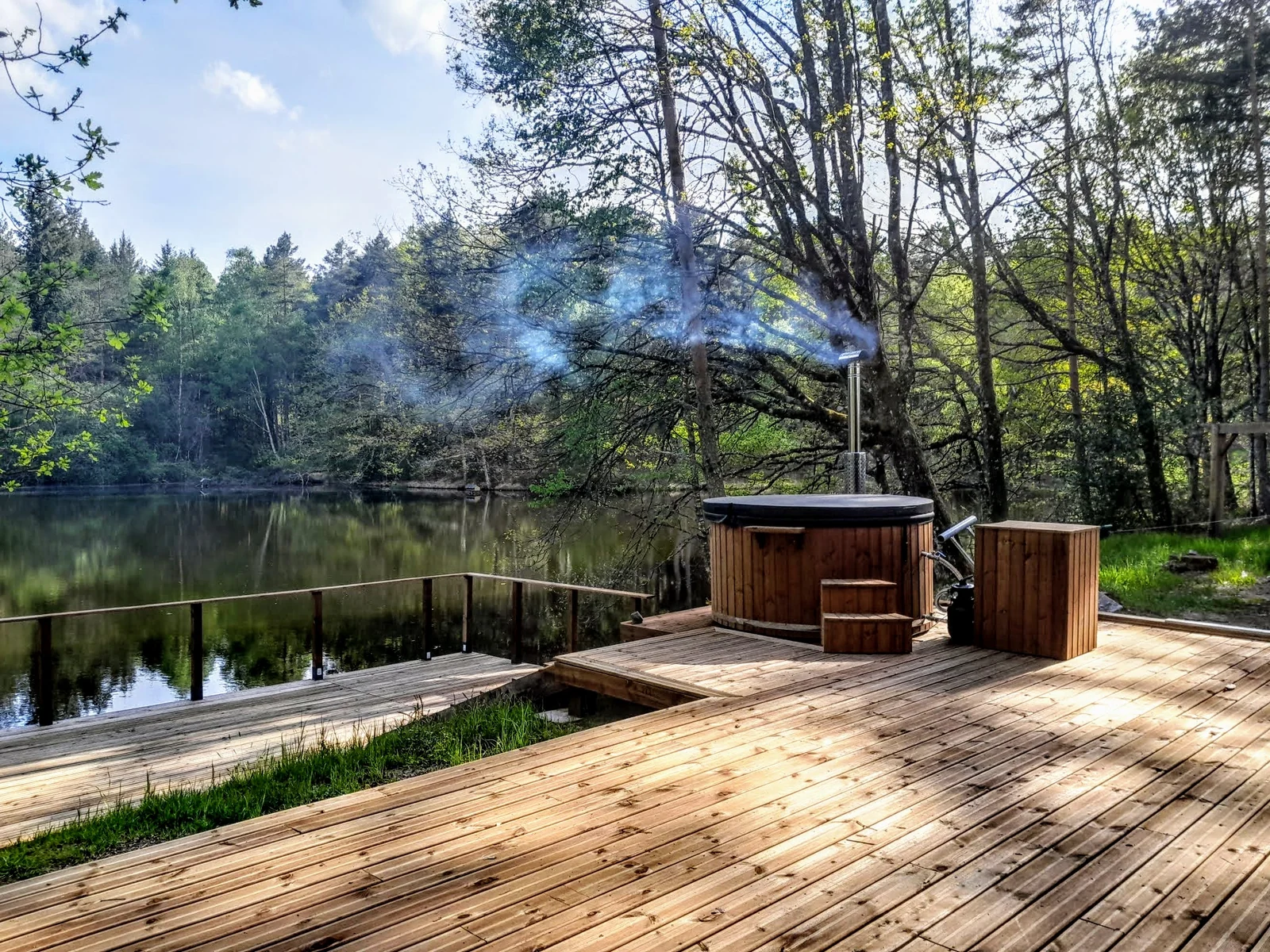 Houten hottub op een terras bij water en bomen