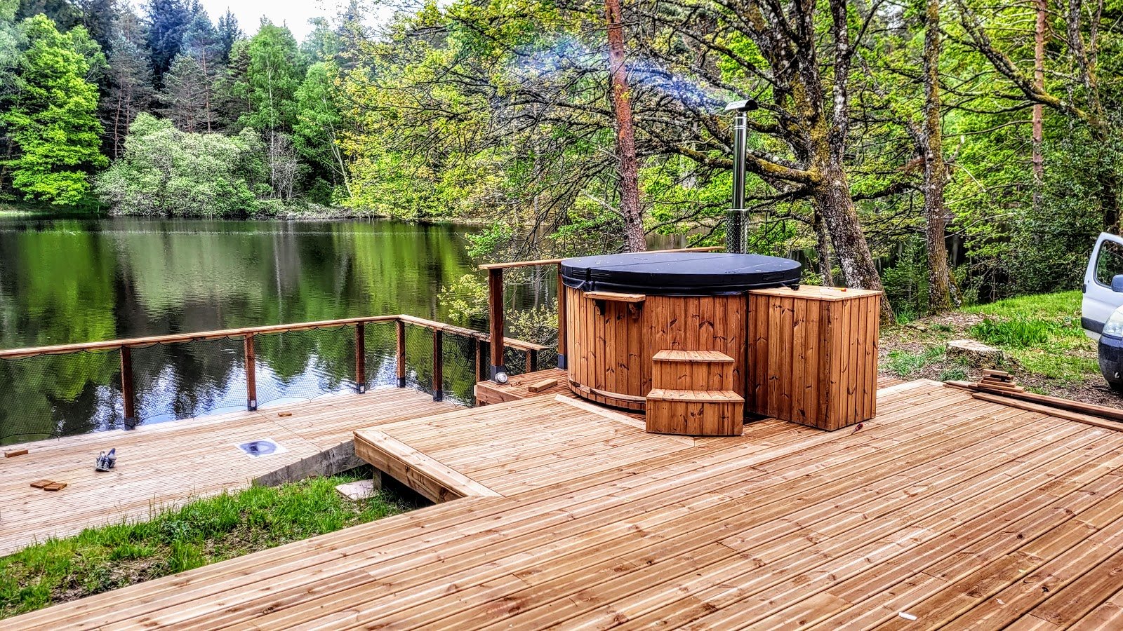 Ronde houten hottub met afdekking en kachel op een terras aan het water