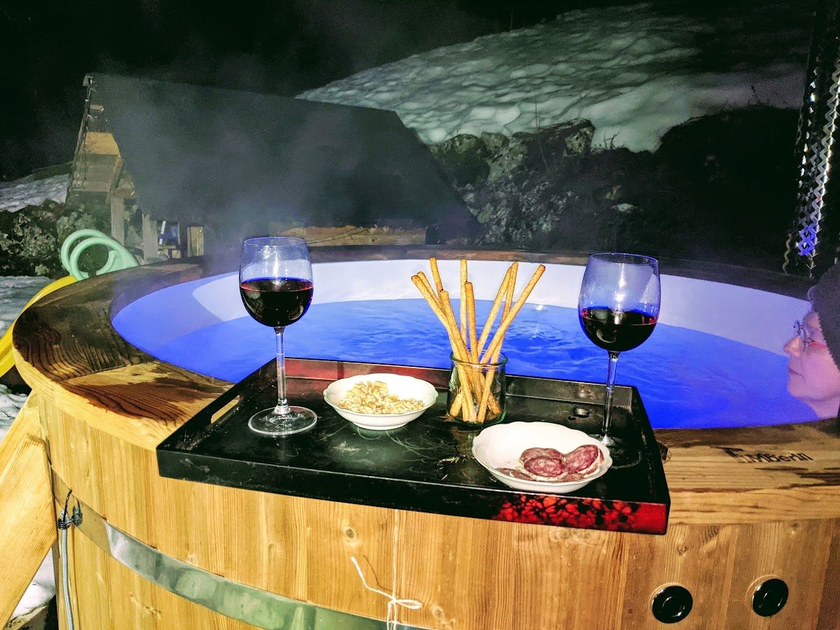 Houten hottub met blauw verlicht water en een dienblad aan de rand tijdens een avond buiten