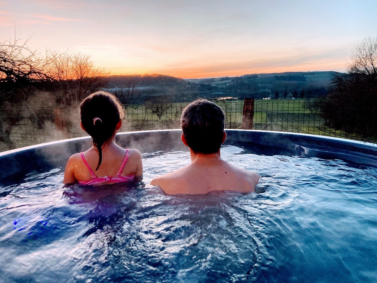 Twee personen ontspannen in een stomende hottub bij zonsondergang met uitzicht over het landschap