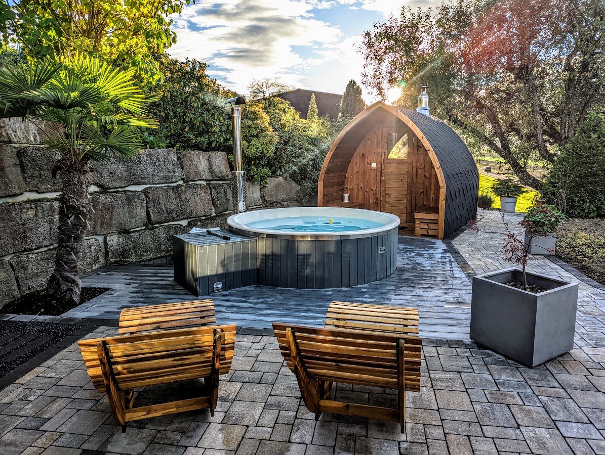 Houten podsauna met beschutte ingang naast een hottub op een groen omringd terras