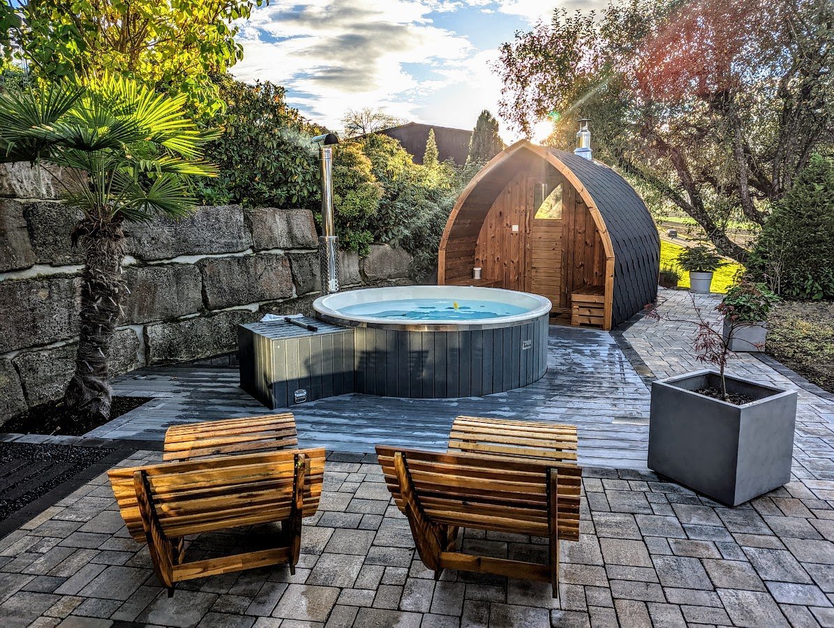 Pod-sauna naast een hottub in een aangelegde tuin met houten stoelen